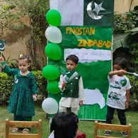 Montessori children hold Pakistan flags beside their Independence Day display board