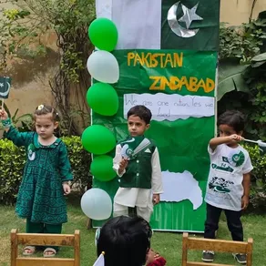 Montessori children hold Pakistan flags beside their Independence Day display board