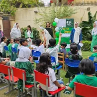 Students raise their hands during an outdoor Independence Day assembly in the school garden