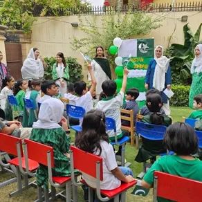 Students raise their hands during an outdoor Independence Day assembly in the school garden