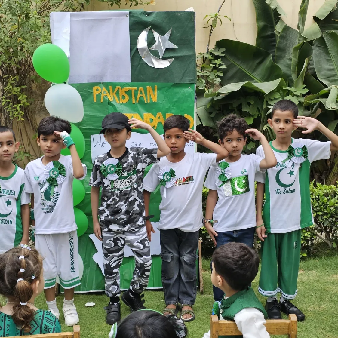 Young Spring Buds students salute in front of a Pakistan Zindabad display on Independence Day