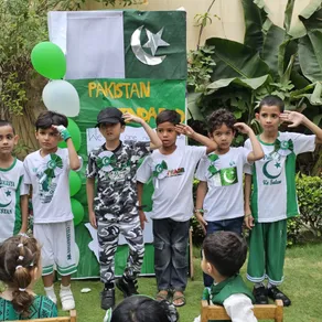 Young Spring Buds students salute in front of a Pakistan Zindabad display on Independence Day